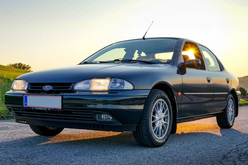 Black Ford sedan parked outdoors, sun shining through windows creating vibrant reflections.
