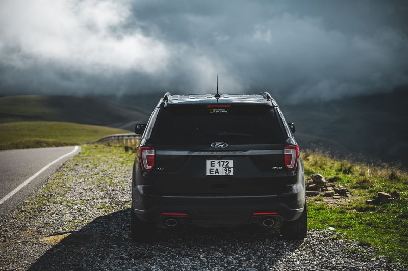 Black SUV parked on a gravel roadside with dramatic cloud-covered mountains.