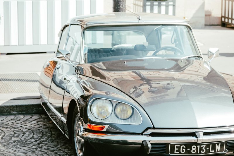 A vintage grey Citroen sedan parked on stone pavement with reflective shine.