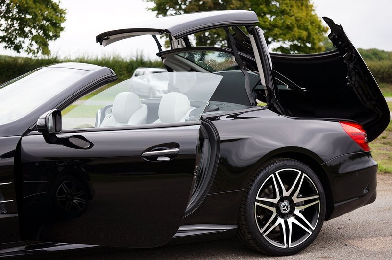 Side view of a sleek black Mercedes convertible car with doors and roof open, showcasing luxurious design.