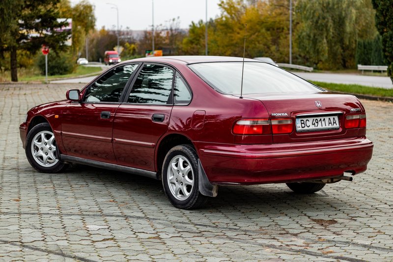Red Honda Accord parked outdoors on cobblestone street in autumn.