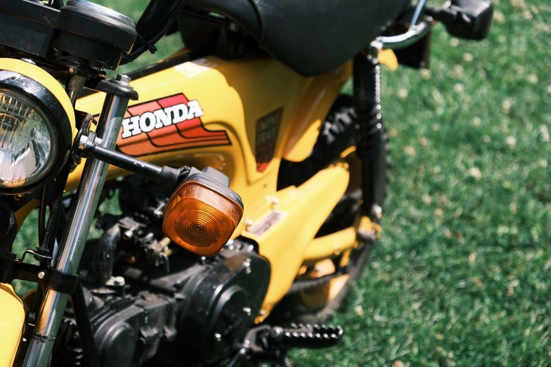 Close-up shot of a classic yellow Honda motorcycle with distinctive features in a grassy setting.