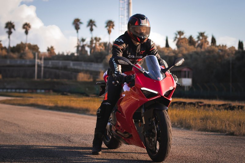 A rider on a red Ducati Panigale motorbike on an open road in Italy.