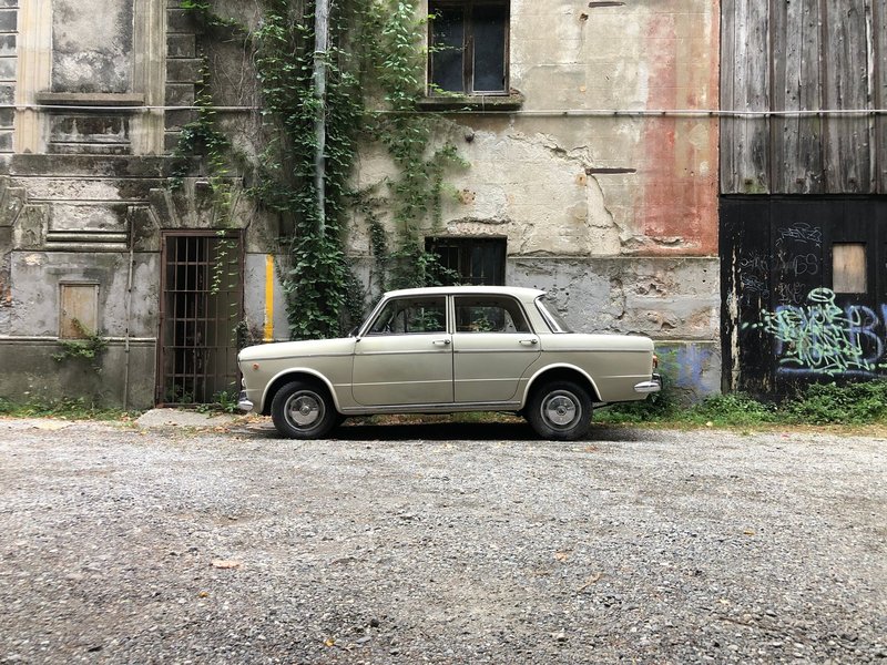 A classic beige Fiat sedan parked in a rustic alleyway in Como, Italy.