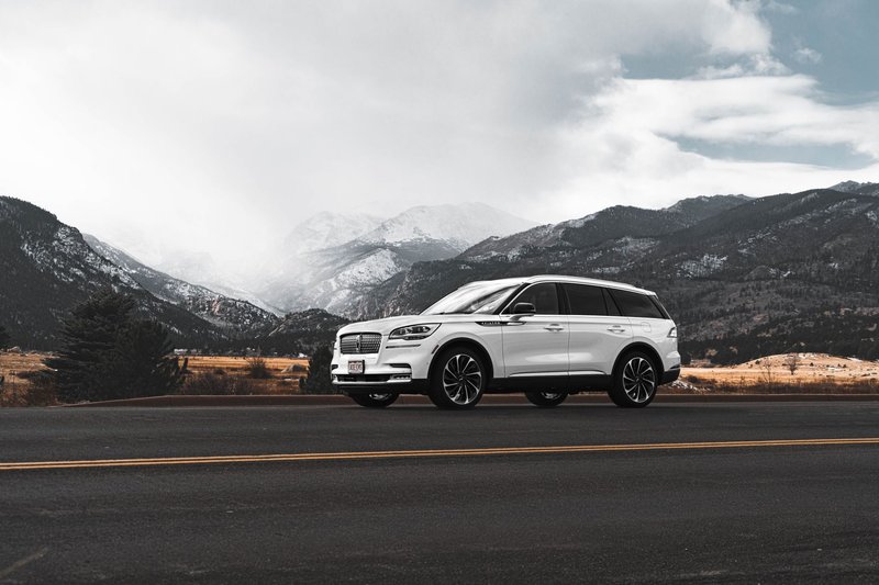 White SUV on a scenic Colorado mountain road with dramatic skies and snowy peaks.