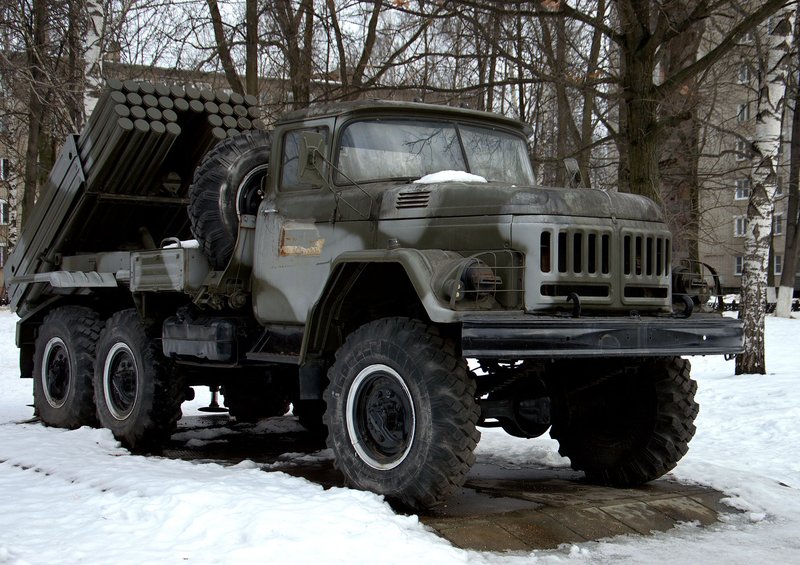 A military cargo truck parked in a snowy outdoor area, surrounded by trees.
