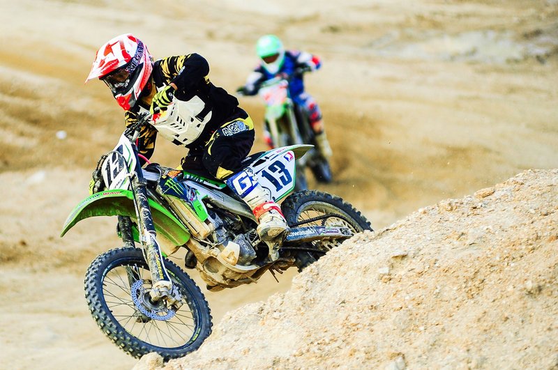 Two motorcyclists racing on a sandy track showcasing speed and skill.