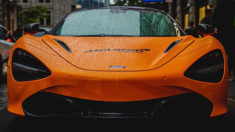Front view of a McLaren 720S with raindrops in an urban setting, showcasing luxury car design.