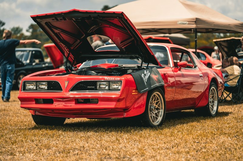 Vintage red Pontiac Trans Am with hood open on display at an outdoor car show.