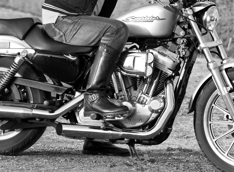 A fashionable motorcyclist in leather boots on a classic Harley-Davidson.