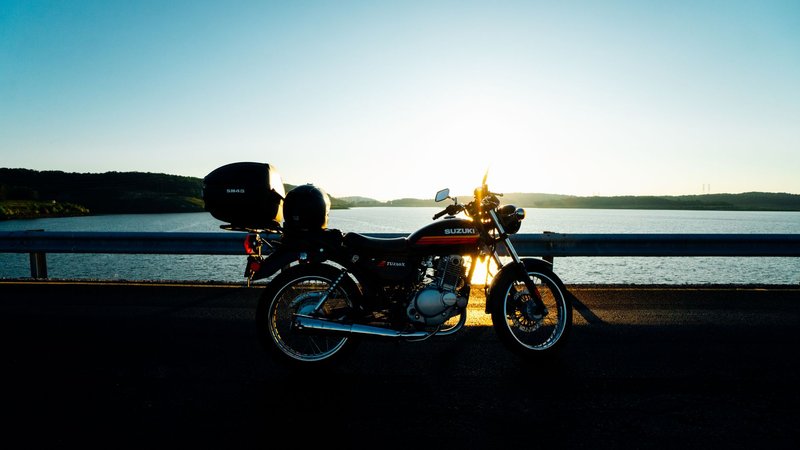 A classic Suzuki motorcycle parked by a tranquil lake during sunset.
