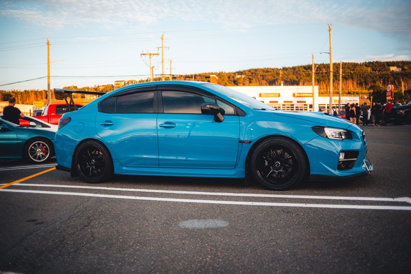 A striking blue Subaru WRX STI sports car parked in a lot during a scenic sunset, showcasing automotive elegance.