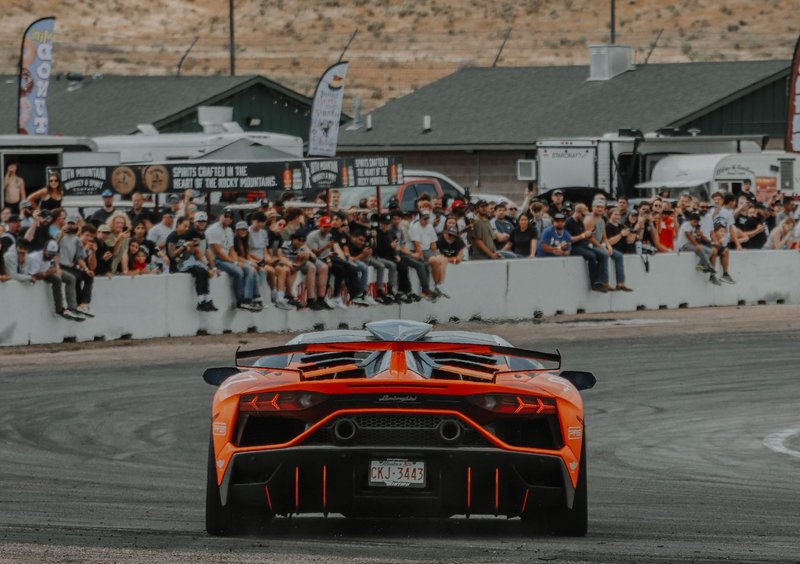 A stunning orange Lamborghini Aventador speeds at a race track with spectators in the background.