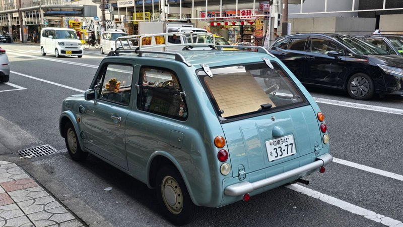 Retro blue car parked on a Japanese street with urban backdrop.