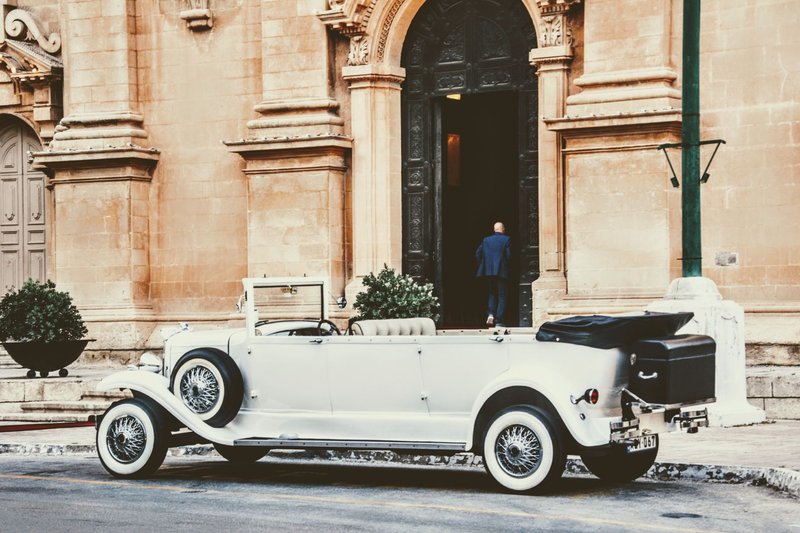A classic white vintage car parked outside a historic church, capturing timeless elegance.