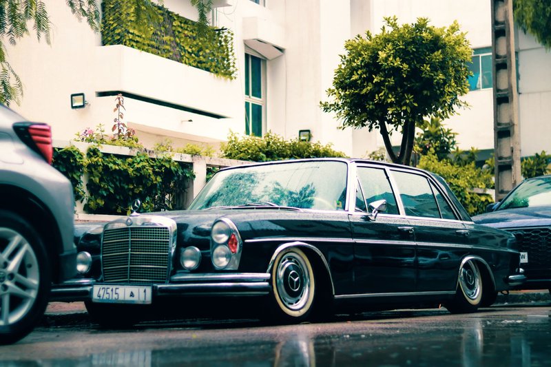 A classic black Mercedes-Benz W108 parked on a rainy city street, showcasing luxury and retro elegance.