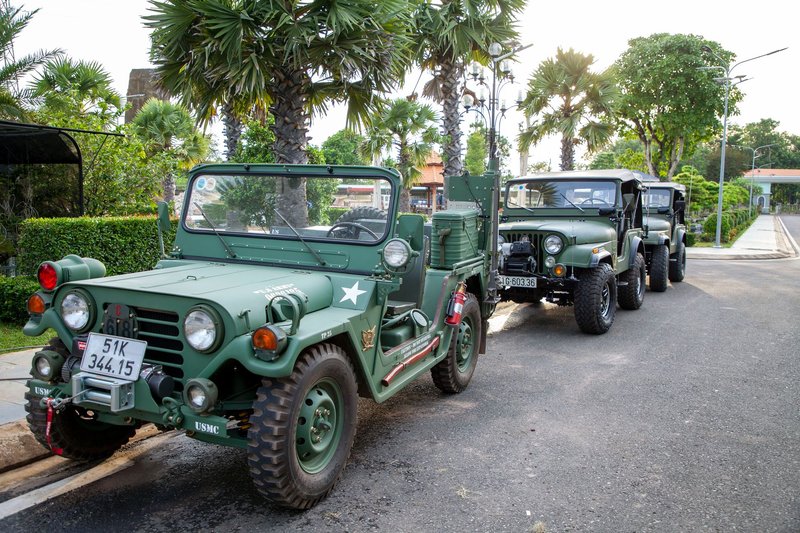 Vintage military jeeps lined up on a street surrounded by tropical foliage, showcasing army vehicles.
