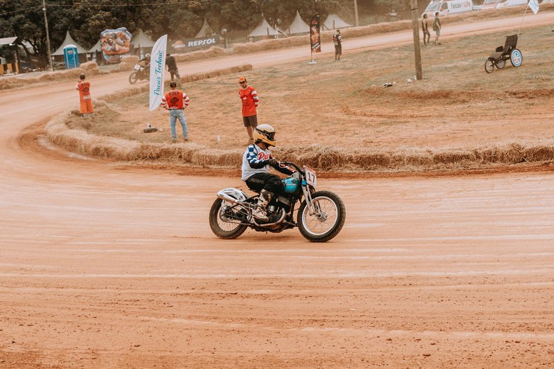 Exciting vintage motorcycle race on a dusty dirt track with spectators and officials in vibrant gear.