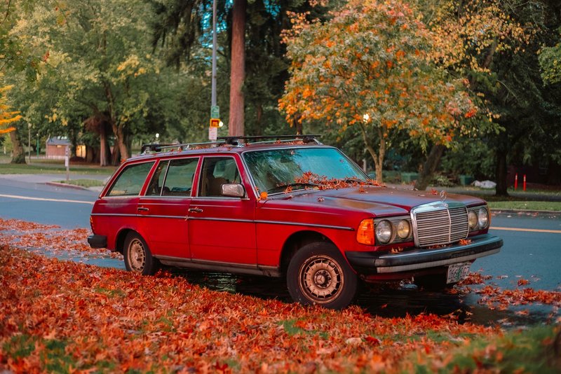 Vintage red car parked on a fall road with colorful autumn leaves.