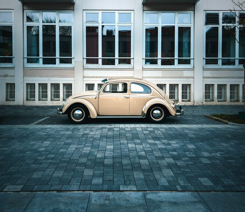 Side view of a classic beige Volkswagen Beetle parked in front of a building.