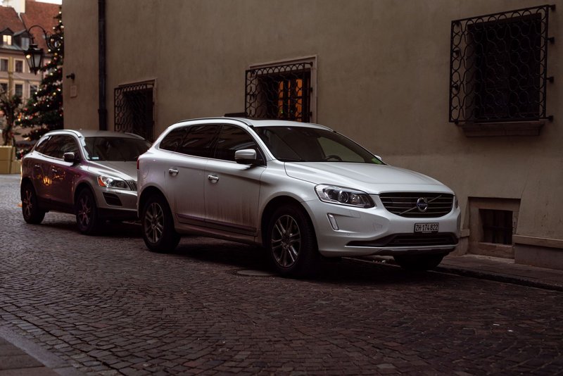 White Volvo SUV parked on cobblestone city street during winter with Christmas decorations.