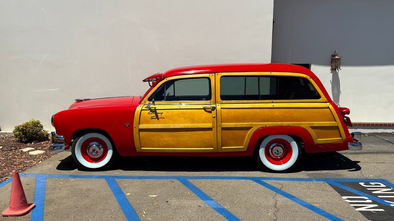 Side view of a classic red and yellow vintage woody wagon parked outdoors on a sunny day.