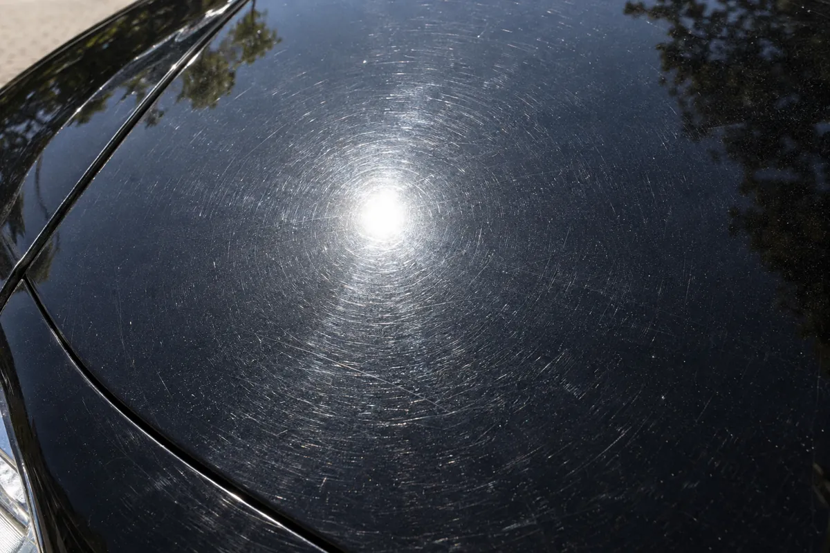 Circular swirl marks around the sun reflection on a black car hood