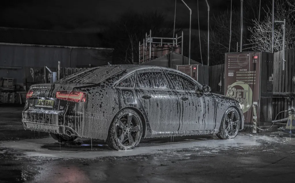 Sedan covered in thick white foam from a foam cannon at a self-service car wash