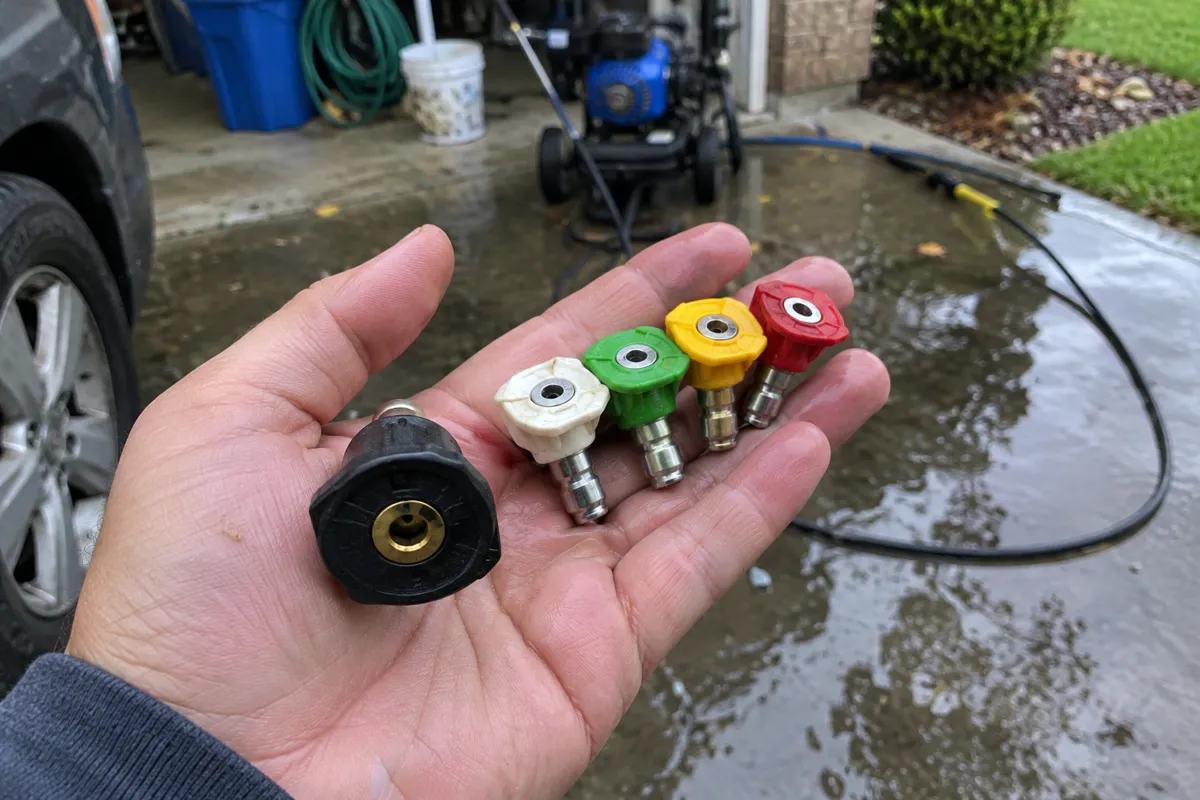 Black soap nozzle held next to white, green, yellow and red pressure washer tips in an open hand
