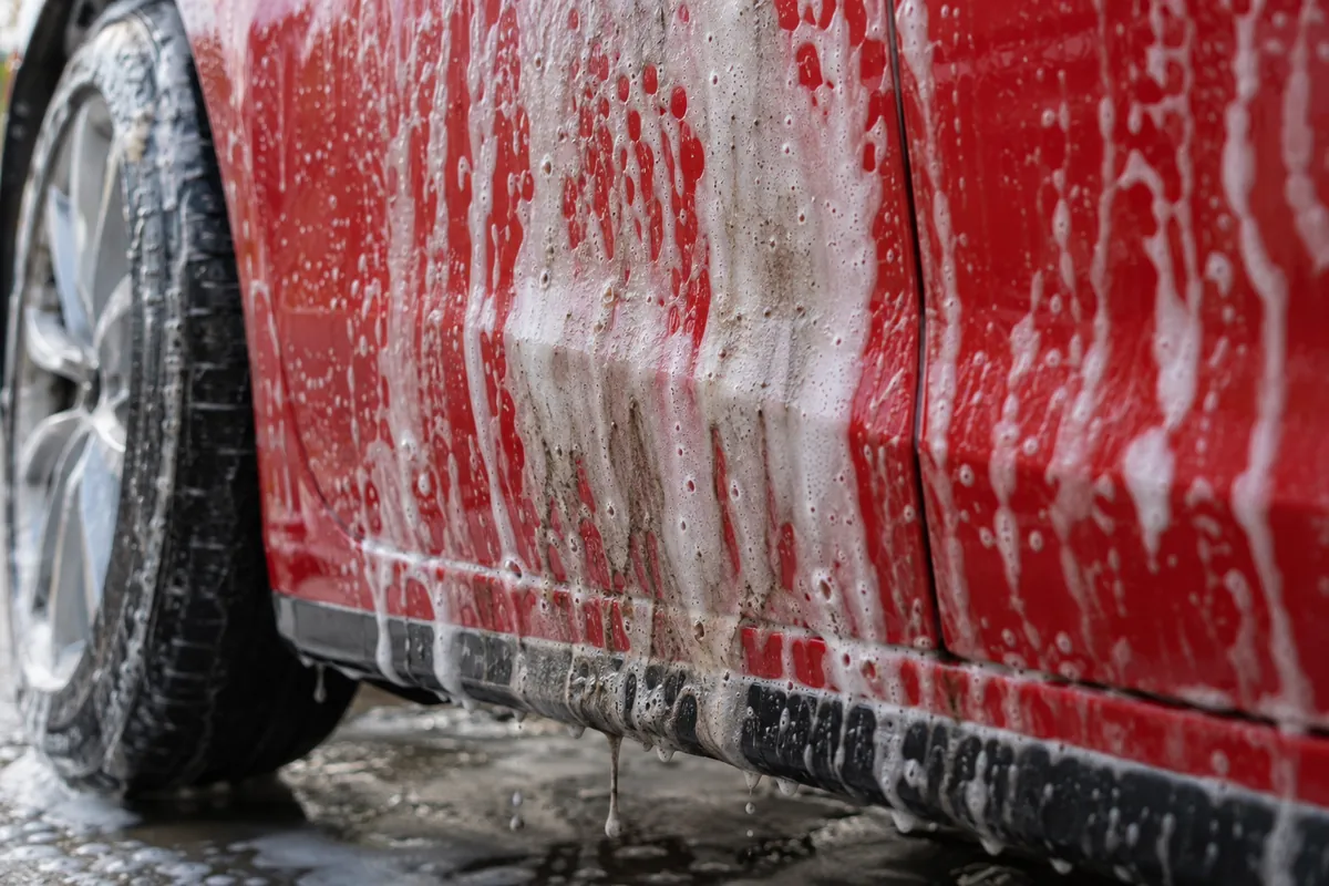 Car wash foam running down a red car door and carrying road grime toward the rocker panel
