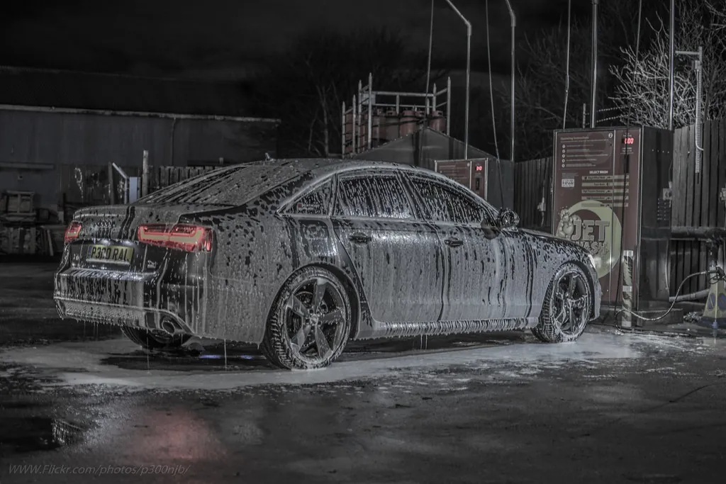 Dark sedan in a wash bay covered in thin, runny snow foam